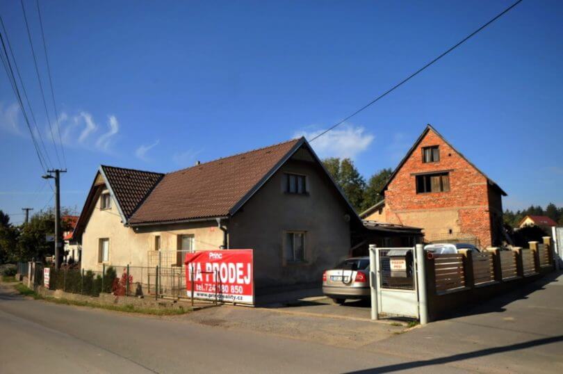 rodinný dům se sedlovou střechou, vjezd na pozemek a hrubá stavba rodinného domu