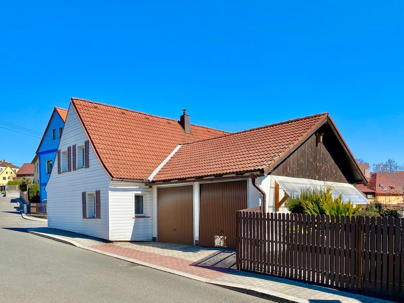 rodinný dům se sedlovou střechou, garážová vrata a plot, modrá obloha