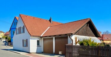 rodinný dům se sedlovou střechou, garážová vrata a plot, modrá obloha