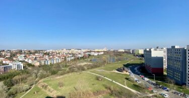 Lužiny, výhled na Prahu, zelená louka, rybníky, panelové domy a rodinné domky, modrá obloha